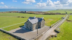 A stone house with a gravel driveway, surrounded by green fields and a clear sky.