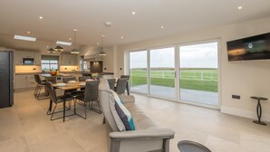 A modern kitchen with a dining area, large windows, and a flat-screen TV.