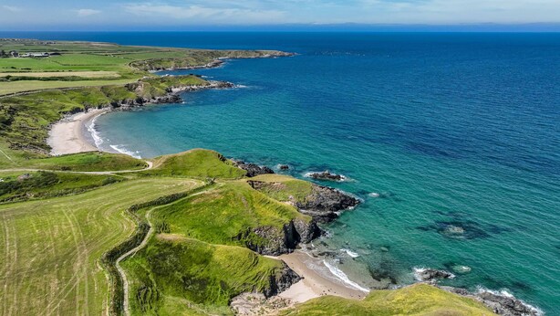 A coastal landscape with a beach, grassy fields, and a clear view of the ocean.