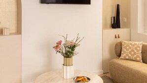 A modern living room with a round marble coffee table, a flat-screen TV mounted on the wall, a vase with flowers, and a sofa with patterned cushions. - Appartement 2 chambre la fayette gare du nord - 4p (Paris)