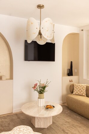 Ein modernes Wohnzimmer mit einem runden Marmortisch, einem flachbildfernseher an der Wand, einer Vase mit Blumen und einer Couch mit gemusterten Kissen.
