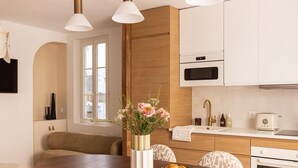 A modern kitchen with a wooden dining table, four patterned chairs, pendant lights, and a vase with flowers. - Appartement 2 chambre la fayette gare du nord - 4p (Paris)