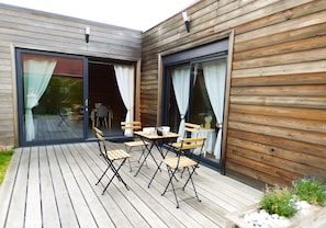 A wooden exterior with sliding glass doors, a patio with outdoor furniture, and a small planter with plants.