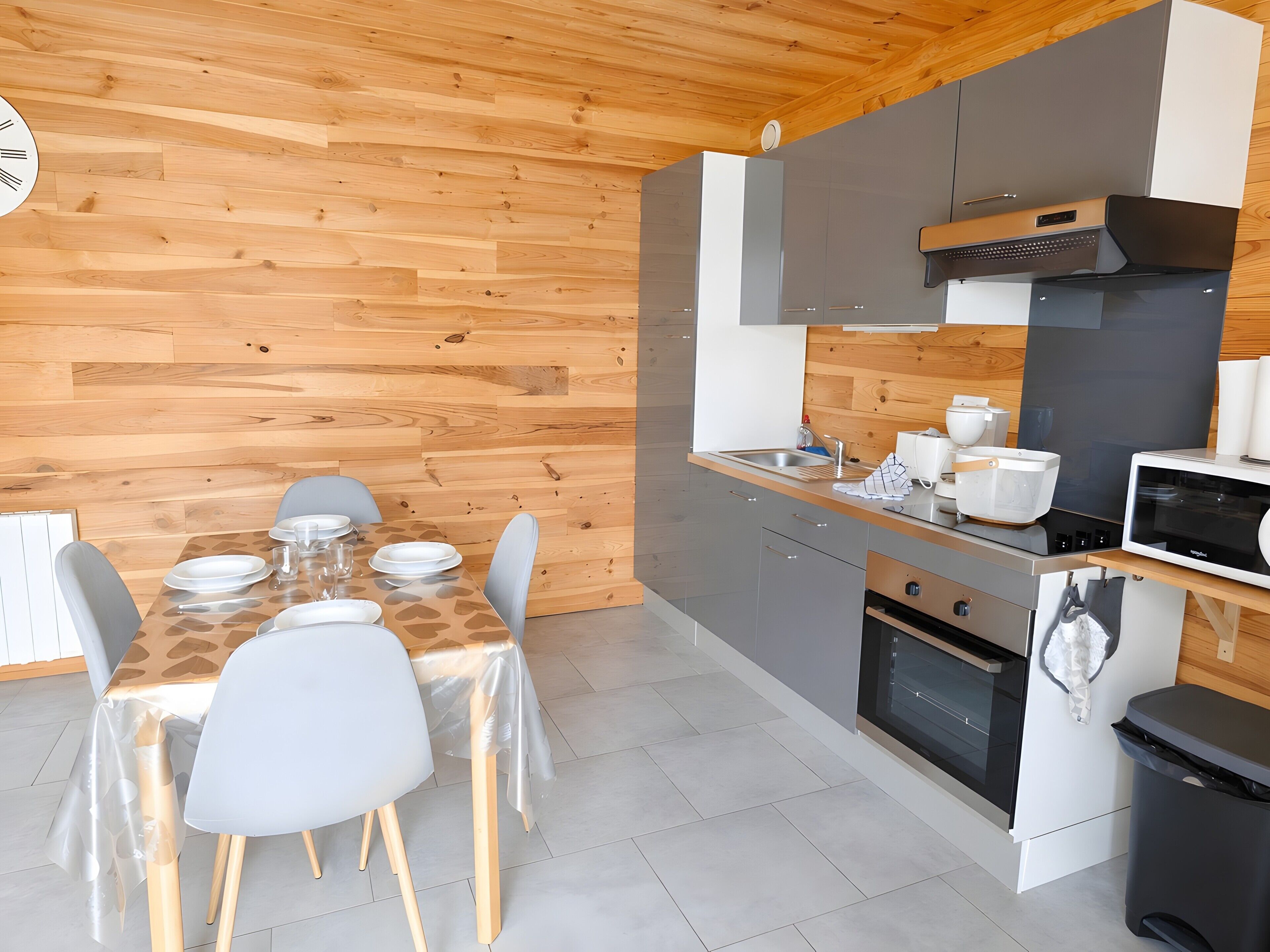 Een moderne keuken met houten lambrisering, een eettafel gedekt met borden en glazen, en een magnetron.