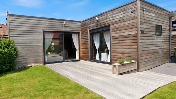 A modern house with a wooden exterior, large sliding glass doors, and a wooden deck. - Chalet 'Le Ch'ti  Lecelles' with Private Terrace and Private Garden (Lecelles)