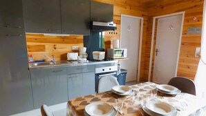 A compact kitchen with modern appliances, a dining area with heart-patterned tablecloths, and wooden paneling. - Chalet 'Le Ch'ti  Lecelles' with Private Terrace and Private Garden (Lecelles)