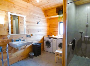 Une salle de bain rustique, situĂ©e dans une cabane en bois, et Ă©quipĂ©e dâun lavabo, dâun miroir, dâune machine Ă laver et dâune douche.