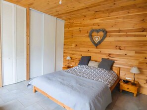Une chambre Ă coucher avec une tĂȘte de lit en bois, un lit recouvert dâune literie Ă motifs, des tables de chevet avec des lampes et une armoire avec des portes coulissantes.