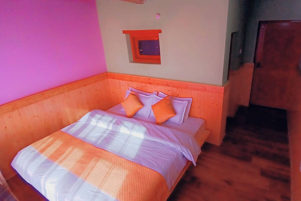 A bedroom with a bed, pillows, a small window, and a door.
