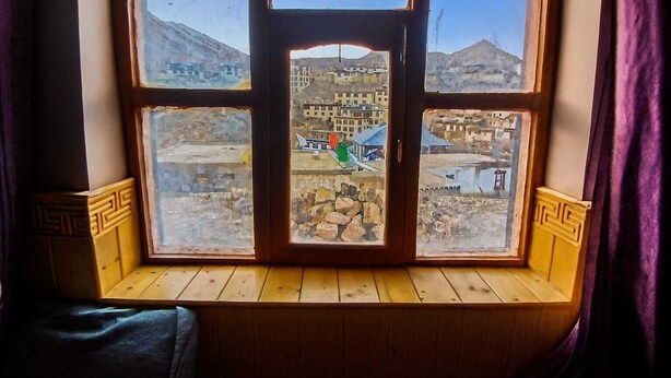 Ein Fenster mit Blick auf eine gebirgige Landschaft und Gebäude.