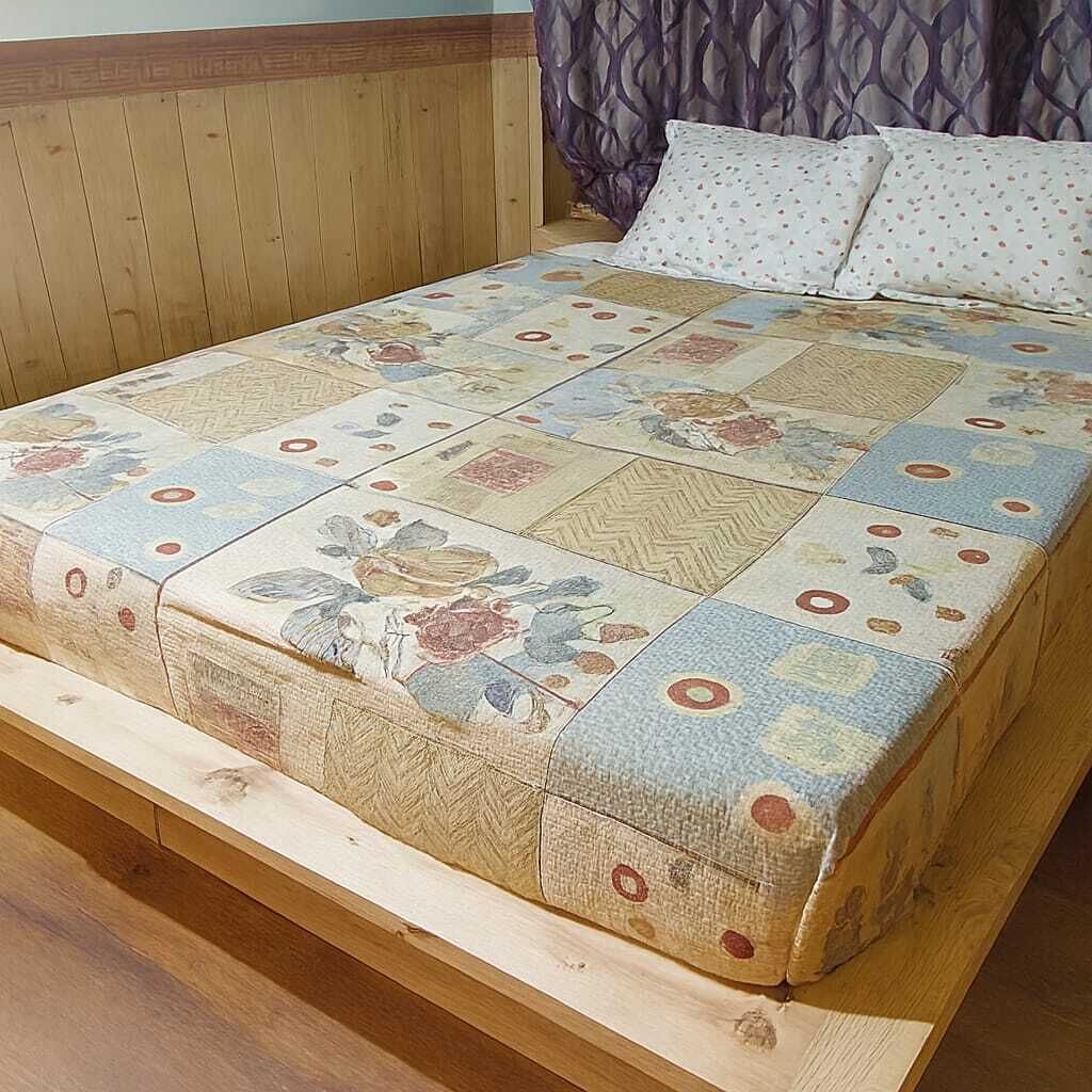 Una cama con una colcha estampada con motivos florales, cabecero de madera y una cortina morada.