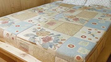 Una cama con una colcha estampada con motivos florales, cabecero de madera y una cortina morada.