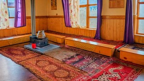 Ein traditionell eingerichteter Raum mit Holzbänken, einem Ofen und gemusterten Teppichen.
