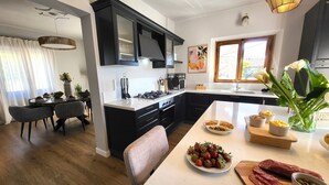 Et moderne køkken med sorte skabe, en hvid bordplade og et spiseområde med et bord og stole.
