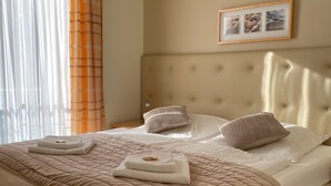 A neatly made bed with a beige quilt, pillows, and a folded towel.