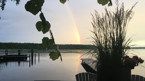 A dock with a chair, a potted plant, and a view of a lake with a rainbow.