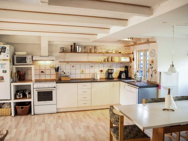 A modern kitchen with white cabinets, a microwave, stove, and a dining area with a table and chairs. - 6 Person Holiday Home in Samso (Samsø)