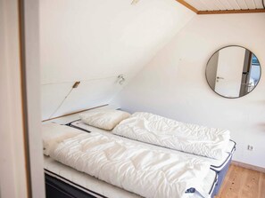A single bed with a white duvet in a room with a wooden floor and a round mirror on the wall. - 6 Person Holiday Home in Samso (Samsø)