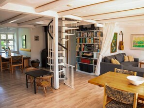 A spacious living area with a wooden floor, a staircase leading to a loft, a bookshelf filled with books, and a guitar on the wall. - 6 Person Holiday Home in Samso (Samsø)