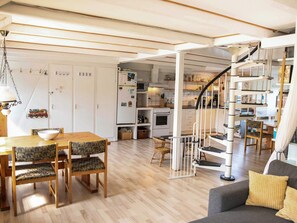 Ein geräumiger Wohnbereich mit einem Holzessttisch, Stühlen, einer Couch, einer Treppe und einer Küche im Hintergrund.