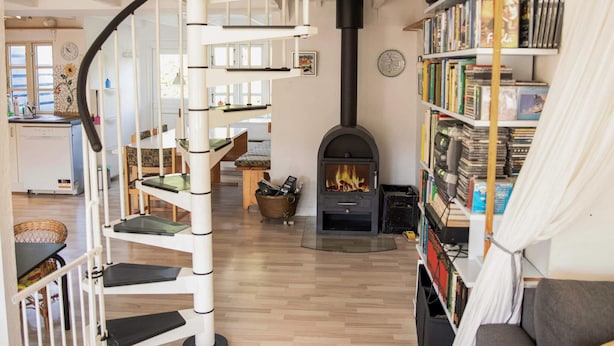 A spiral staircase, a fireplace, and a bookshelf in a room with wooden flooring. - 6 Person Holiday Home in Samso (Samsø)