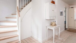 Eine Treppe mit Holzboden und weißen Wänden, ein weißes Schränkchen mit Dekorationen und ein kleiner Tisch mit Teekanne.