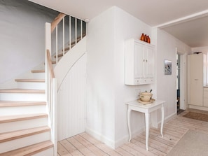 Eine Treppe mit Holzboden und weißen Wänden, ein weißes Schränkchen mit Dekorationen und ein kleiner Tisch mit Teekanne.