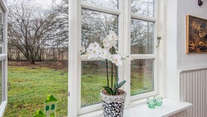 Ein Fenster mit weißen Orchideen, einer Topfpflanze und einem kleinen grünen Spielzeughaus.