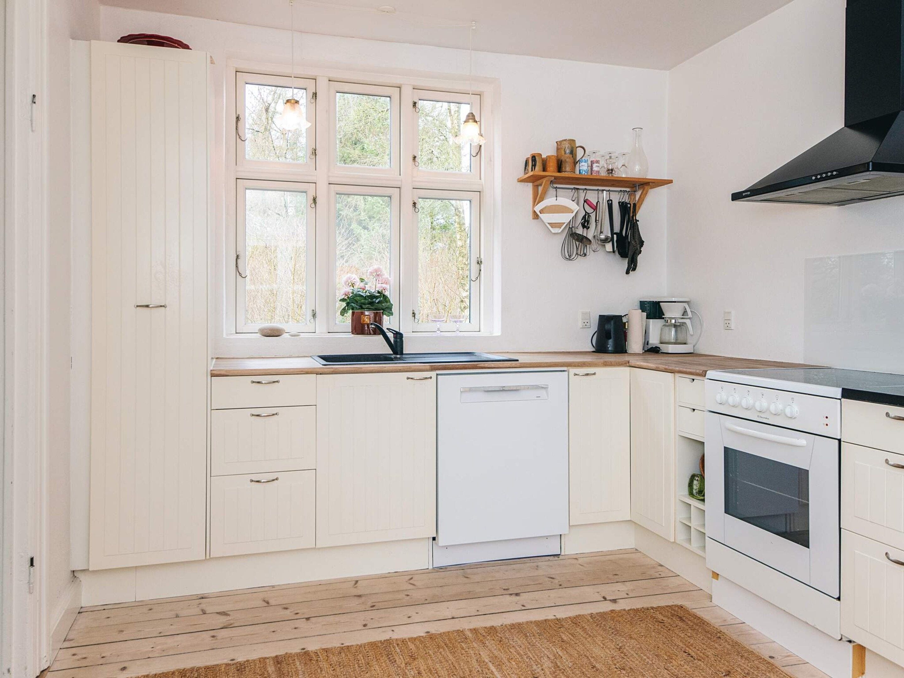 A kitchen with white cabinetry, a dishwasher, a stove, and a window with a view of trees.