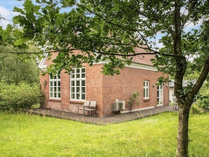 Un bâtiment en briques avec de nombreuses fenêtres, un petit porche et un arbre au premier plan.
