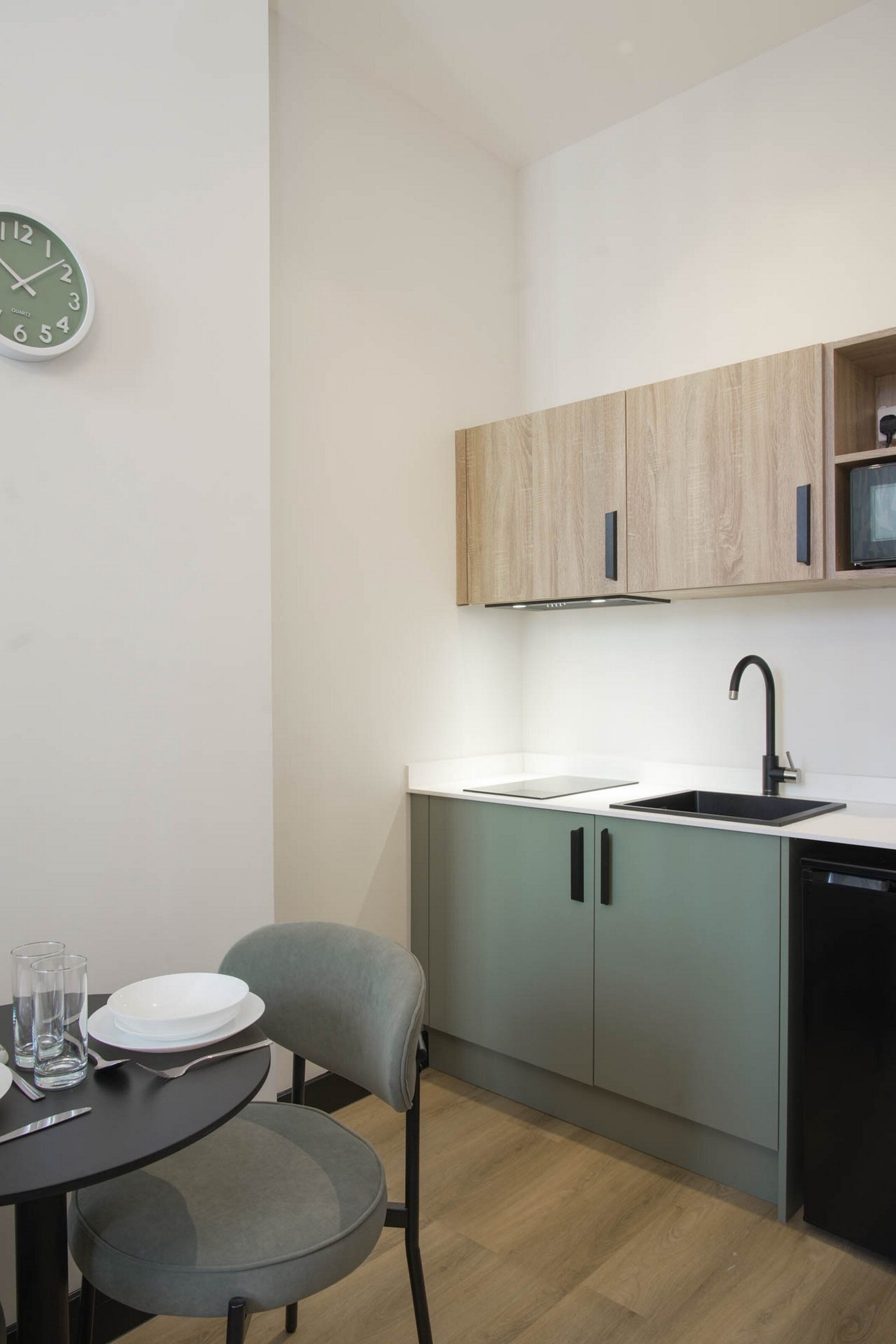 A compact kitchen with a sink, cabinets, and a clock on the wall.