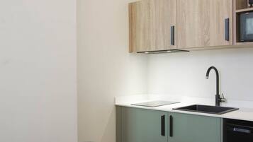 A compact kitchen with a sink, cabinets, and a clock on the wall.