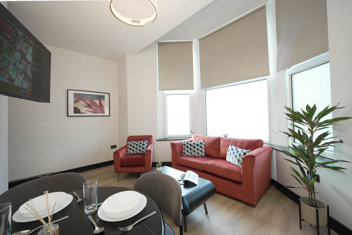Ein modernes Wohnzimmer mit Esstisch für zwei Personen, einem roten Sofa und einem großen Fenster, das natürliches Licht hereinlässt.