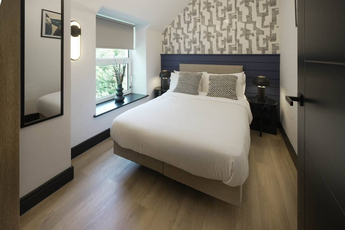 Ein modernes Schlafzimmer mit einem großen Bett, einem gemusterten Kopfteil, Nachttischlampen und einem Fenster mit Blick.