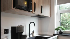 A modern kitchen with a built-in microwave, a coffee machine, a sink, and a window with a view of greenery. - The Sixty 19 Stylish Studios and Apt. (Cardiff)