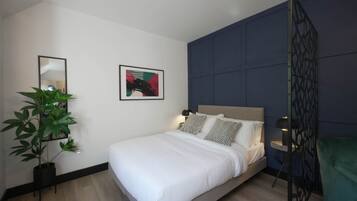 A modern bedroom with a bed, a potted plant, a framed picture, and a decorative partition.