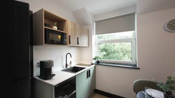 Cocina compacta con cafetera, pileta y ventana con vista a zonas verdes.