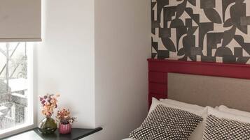 A bedroom with a bed, a window with a view, a wall with a geometric pattern, and a modern light fixture.