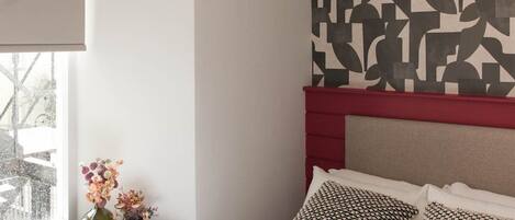 Une chambre à coucher avec un lit, une fenêtre donnant sur un beau paysage, un mur orné d’un motif géométrique et un luminaire moderne.