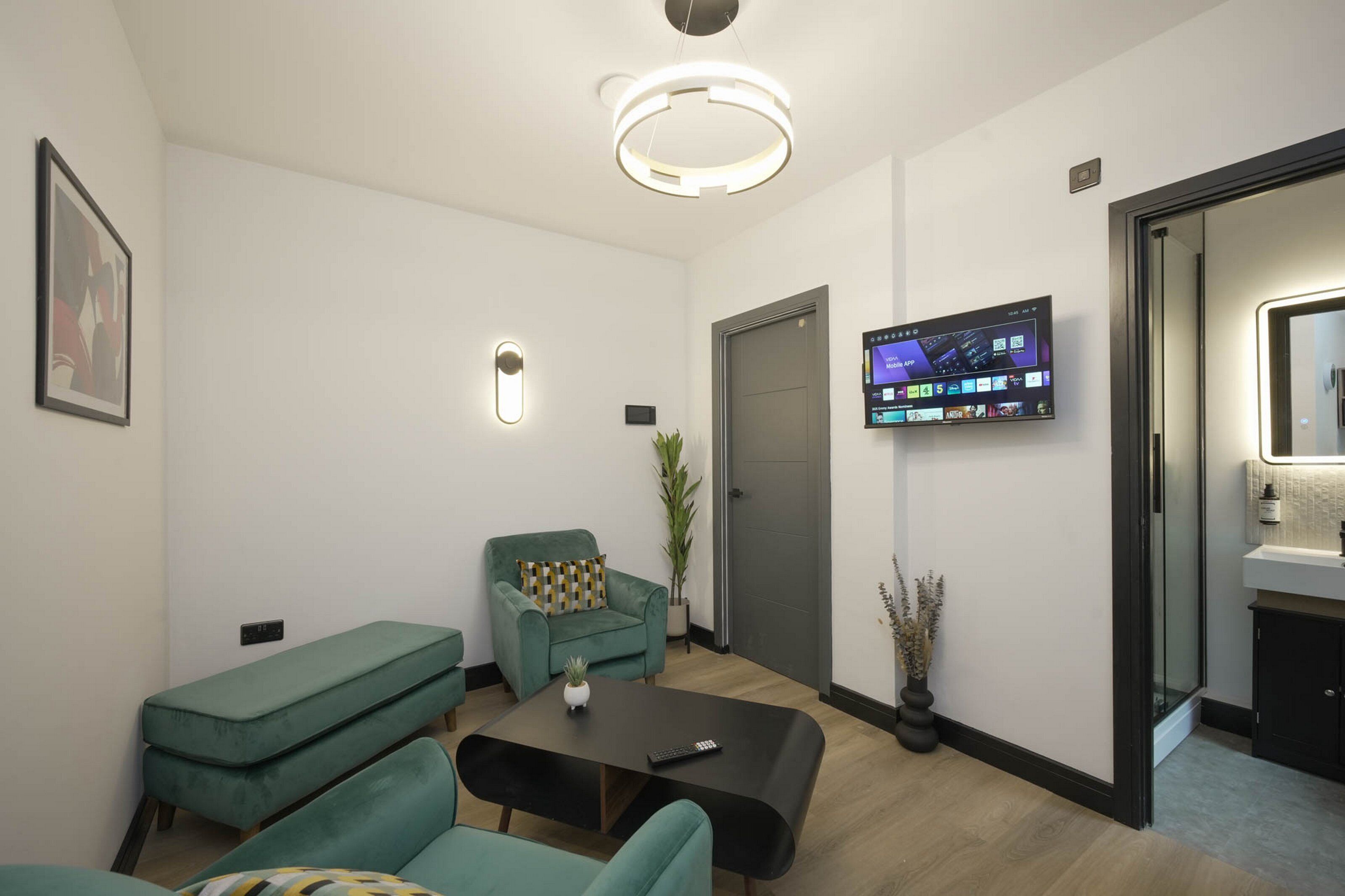 A modern living room with a sofa, a coffee table, a TV mounted on the wall, and a door leading to a bathroom.
