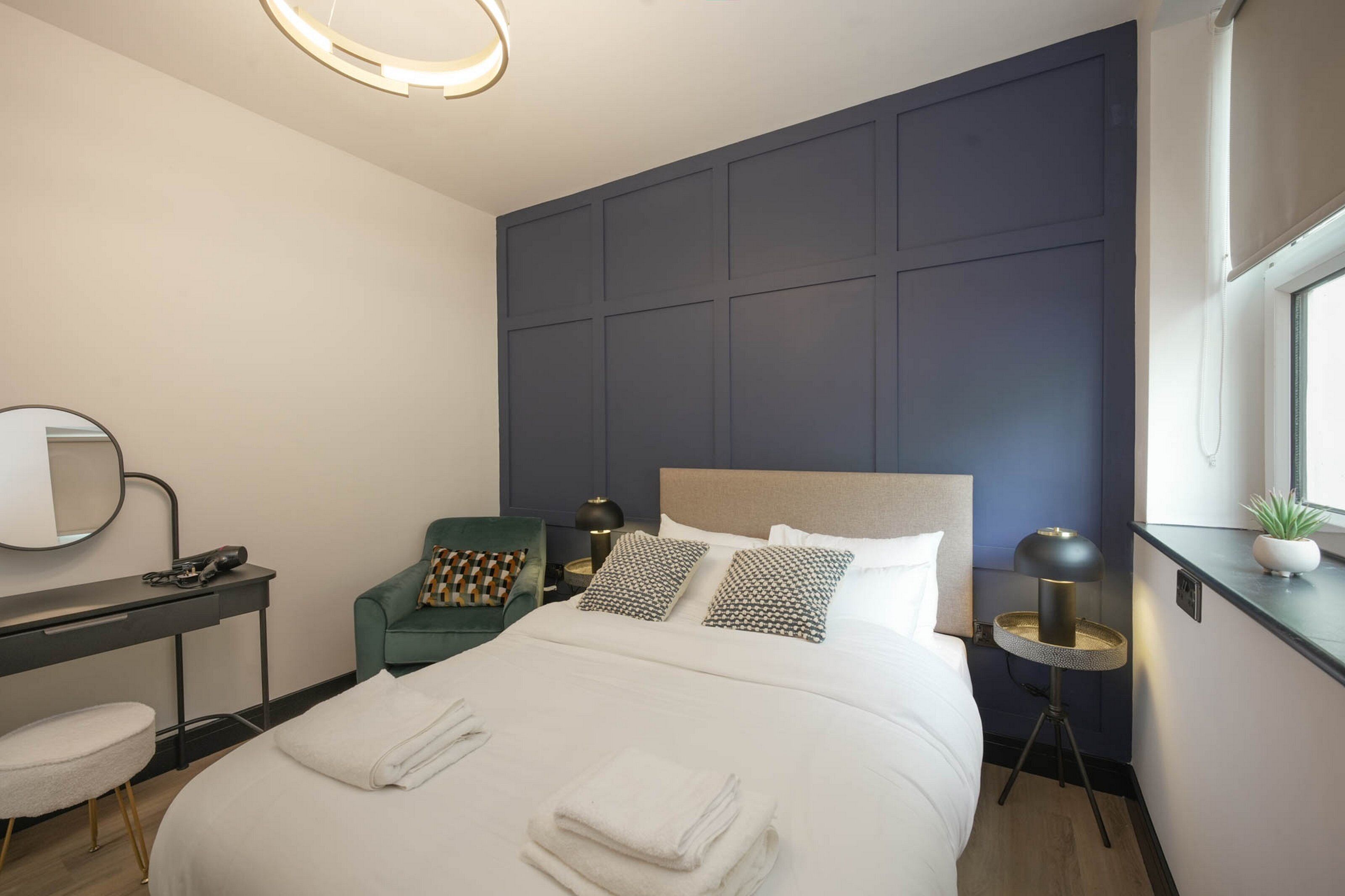 Una habitación de hotel moderna con cama, escritorio, silla, mesita de noche, lámpara y una pequeña planta en maceta.