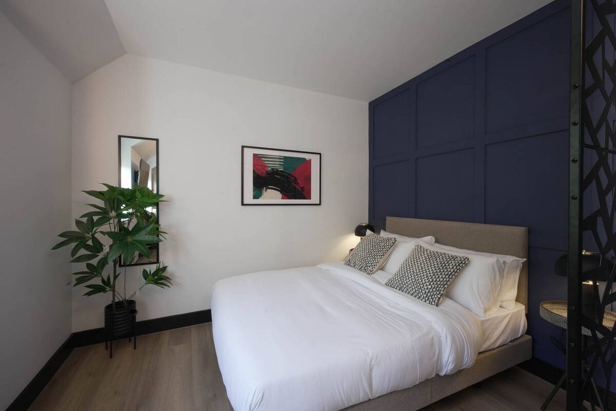 Ein modernes Schlafzimmer mit einem Bett, einer Topfpflanze und zwei gerahmten Kunstwerken an der Wand.