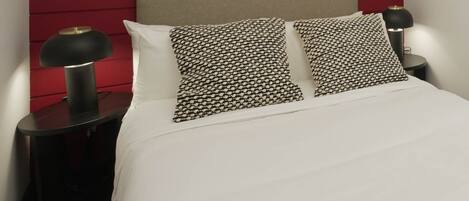 A bed with white bedding, two patterned pillows, a red headboard, and two bedside tables with lamps.