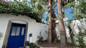 Un bâtiment blanc avec une porte bleue, entouré de verdure et de palmiers.