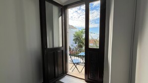Une porte ouverte donnant sur un balcon d’où l’on peut admirer un immeuble et une table bleue placée à l’extérieur.