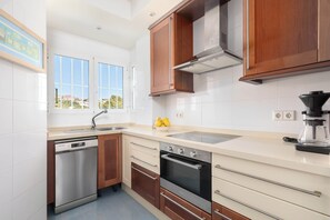 A modern kitchen with stainless steel appliances, wooden cabinets, and a large window offering a view. - Jardines de Calahonda IX | Sea View & Pool (Mijas Costa)