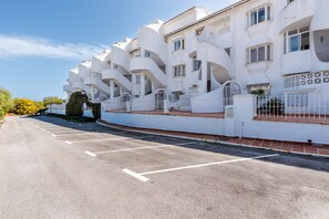 Un bâtiment blanc doté de balcons, un ciel dégagé et un parking.