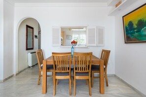 A dining area with a wooden table and chairs, a mirror above the table, and a painting on the wall.