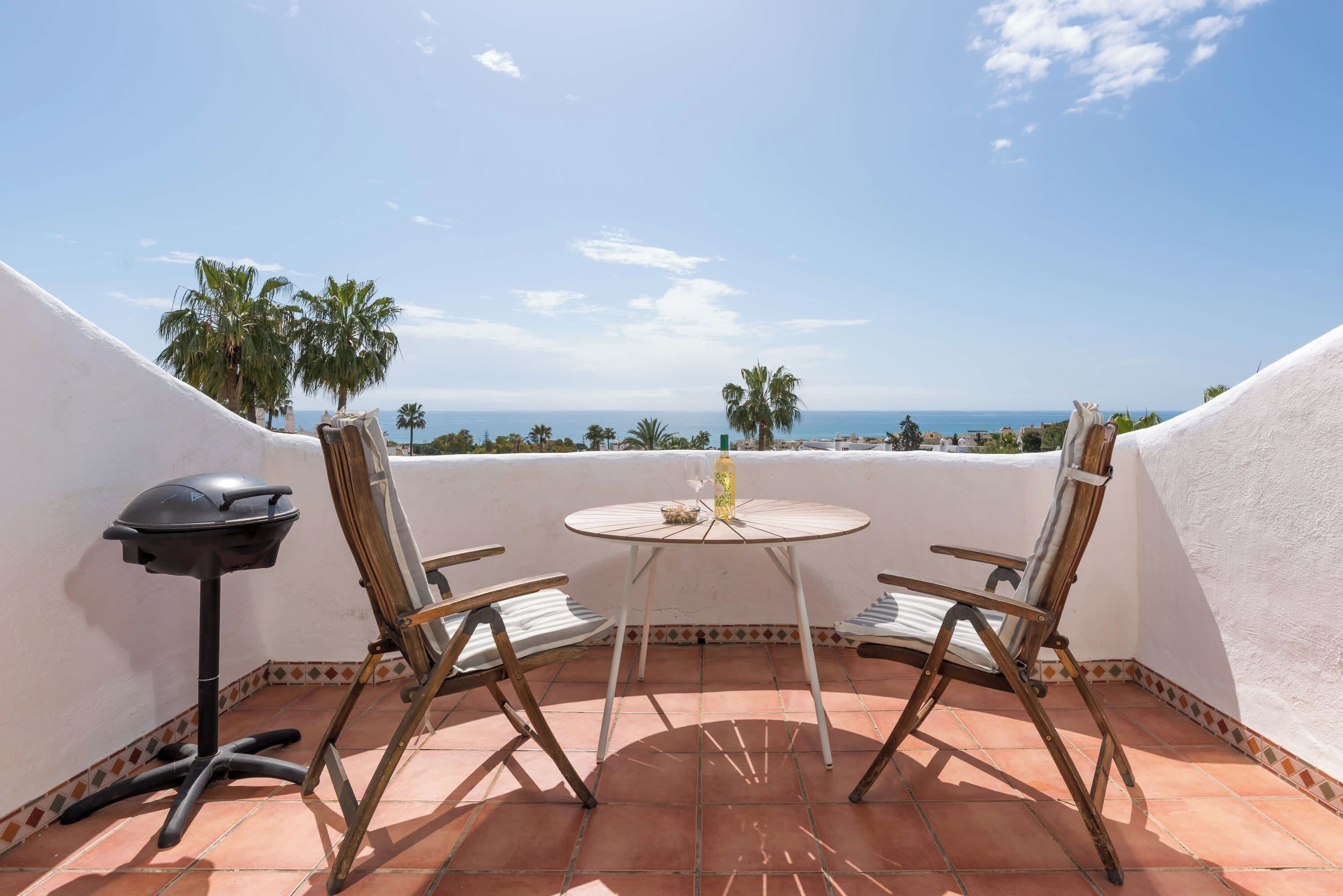 Um terraço com mesa, cadeiras, churrasqueira e vista para o mar.