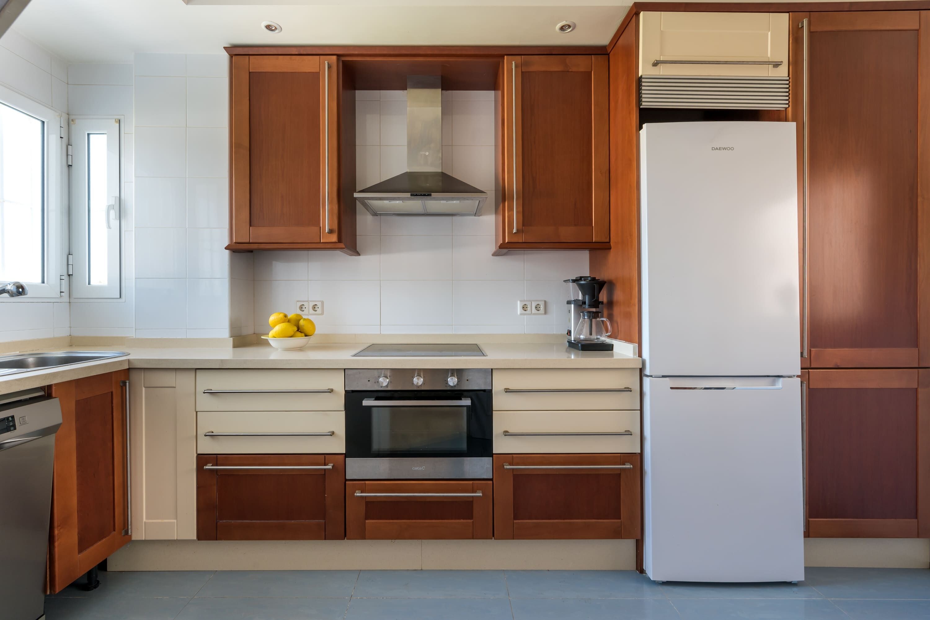 A modern kitchen with wooden cabinets, a stainless steel oven, a built-in dishwasher, and a white refrigerator.